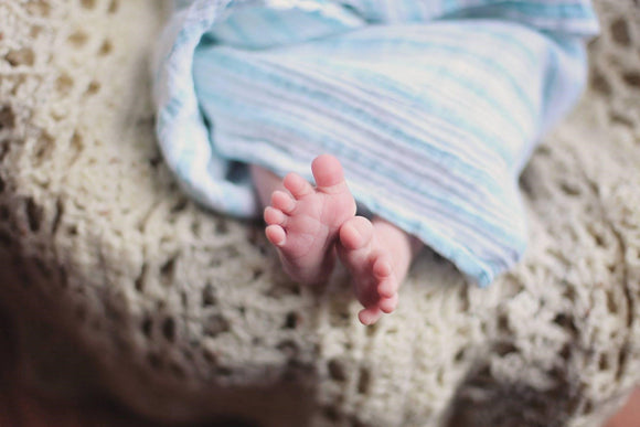 Baby feet peeking out from under a blue striped muslin blanket